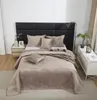 A neatly made bed with a beige quilted bedspread and pillows, set against a black upholstered headboard in a bedroom. Podgląd zdjęcia produktu