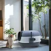 A cat sits next to a large, enclosed litter box in a well-lit room with a large window showing greenery outside. Náhled obrázku produktu