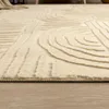 A close-up view of a cream-colored rug with a geometric pattern, placed on a wooden floor. Produktbild-Vorschau