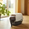 A black and white cat is walking out of a covered litter box in a room with a window and curtains. Produktbild-Vorschau