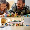 A father and daughter are playing with LEGO bricks, building small models. The bottom half of the image shows the completed models laid out on a wooden floor. Podgląd zdjęcia produktu