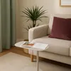 A beige organic side table with a book on it, placed next to a sofa with a burgundy cushion and a potted plant. Produktbild-Vorschau