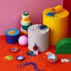 A collection of colorful geometric shapes and small decorative pieces arranged on a red surface against a pink background. Anteprima dell’immagine prodotto