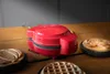 A red waffle maker is on a wooden table, with several waffles around it. Produktbild-Vorschau