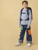 A young girl wearing a backpack and jeans stands against a plain yellow background. Anteprima dell’immagine prodotto