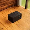 A black cat house is placed on a wooden floor next to a window and wooden cabinets. Produktbild-Vorschau