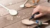 A person's hand is using a Dremel tool to carve a wooden spoon on a wooden workbench. Anteprima dell’immagine prodotto