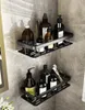 Two black shower shelves are mounted on a tiled wall, holding various bottles of toiletries and personal care items. Produktbild-Vorschau