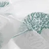 A close-up view of white sheer curtains with embroidered teal leaf patterns. Produktbild-Vorschau
