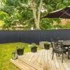 A backyard scene with a wooden deck, patio furniture, potted plants, and a dark gray privacy fence. Produktbild-Vorschau