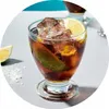 A close-up of a glass filled with a dark beverage, ice, and lime slices. Produktbild-Vorschau