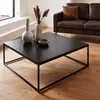 A black metal coffee table is shown in a living room setting, with a brown leather sofa in the background. Anteprima dell’immagine prodotto