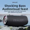 A black portable speaker with colorful LED lights is placed on rocks near the water. Produktbild-Vorschau