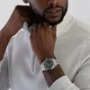 A man is adjusting his sweater collar while wearing a watch. Náhled obrázku produktu