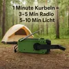 A green hand-crank radio and flashlight sits on the ground in a forest, with a tent in the background. Produktbild-Vorschau