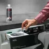 A person is pouring liquid from a small bottle into a washing machine dispenser. Produktbild-Vorschau