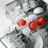 A dishwasher rack filled with kitchenware, including white mugs and orange silicone lids. Podgląd zdjęcia produktu