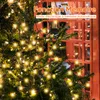A Christmas tree decorated with lights, with a red structure resembling a phone booth in the background. Anteprima dell’immagine prodotto