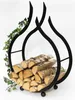 A black metal firewood rack shaped like flames, filled with logs and decorated with ivy. Produktbild-Vorschau