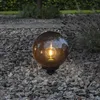 A decorative globe light sits on a gravel path in a garden at dusk. Produktbild-Vorschau