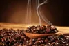 A close-up shot of roasted coffee beans in a wooden spoon, with steam rising. Produktbild-Vorschau