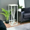 A white metal plant stand with a twisted design is placed next to a dark sofa and a potted plant. Anteprima dell’immagine prodotto