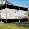 A transparent outdoor curtain is installed on a patio or terrace, attached to a house. The curtain is partially rolled up, revealing patio furniture and a view of trees and sky behind it. The bottom of the curtain has a black opaque strip. Produktbild-Vorschau