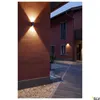 An outdoor wall light illuminates a textured red wall and a paved walkway at dusk. Produktbild-Vorschau