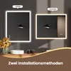 Two illuminated mirrors are displayed side-by-side, showcasing different installation orientations (vertical and horizontal). A vase of sunflowers and a sink are visible on a wooden counter below. Produktbild-Vorschau