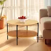 A round, two-tiered coffee table with a wood grain finish and black metal legs, placed in a living room setting next to a sofa and a potted plant. Produktbild-Vorschau