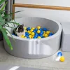 A rabbit sits in a grey ball pit filled with blue and yellow balls. Produktbild-Vorschau
