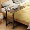 A mobile, height-adjustable bedside table with a laptop, coffee cup, and phone on it, placed next to a bed. Podgląd zdjęcia produktu