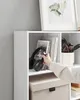 A hand is reaching into a white cube shelf to adjust a pair of black headphones. Produktbild-Vorschau