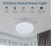 A white motion sensor light is mounted on a white ceiling, with curtains visible below. Produktbild-Vorschau