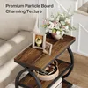 A close-up shot of a rustic brown side table with a metal frame, decorated with framed pictures and a vase of flowers. Anteprima dell’immagine prodotto