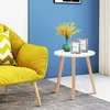 A small round white table with wooden legs is placed next to a yellow armchair in a room with a blue wall. Produktbild-Vorschau