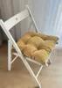 A white folding chair with a mustard yellow cushion is shown in a room with light curtains in the background. Produktbild-Vorschau
