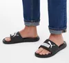 A person's feet wearing black Puma slides and blue jeans. Anteprima dell’immagine prodotto