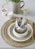 A table setting with plates, cutlery, a glass of wine, and a pitcher with greenery. Produktbild-Vorschau