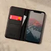A black leather phone case with a red accent is shown open, with a credit card inserted and a smartphone displaying a mountain landscape. Produktbild-Vorschau