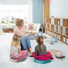 A woman is reading a book to two young girls in a brightly lit room with shelves and toys. Produktbild-Vorschau