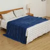 A blue blanket is laid out on a bed with checkered sheets. Produktbild-Vorschau