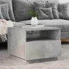 A concrete-look side table with a plant and books on top, placed next to a gray sofa. Produktbild-Vorschau