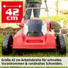 A person is using a red electric lawnmower on a grassy lawn with a stone wall in the background. Produktbild-Vorschau