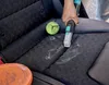 A person is using a handheld cleaning device on a car seat, with a tennis ball and some liquid on the seat. Podgląd zdjęcia produktu