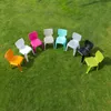 Several colorful plastic chairs are arranged in a semi-circle on a grassy lawn. Produktbild-Vorschau