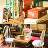 A collage of images showing a miniature dollhouse cafe scene with various details like a menu board, a suitcase, chairs, a table with coffee cups, and a piano. Anteprima dell’immagine prodotto