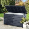 A dark gray outdoor storage box with its lid open, placed on a patio next to a lawn and some trees. Produktbild-Vorschau
