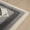A close-up view of a shaggy rug with a geometric pattern in shades of gray and white, laid on a light wooden floor. Produktbild-Vorschau