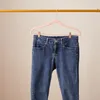 A pair of blue denim jeans hanging on a pink hanger from a gold rod. Produktbild-Vorschau
